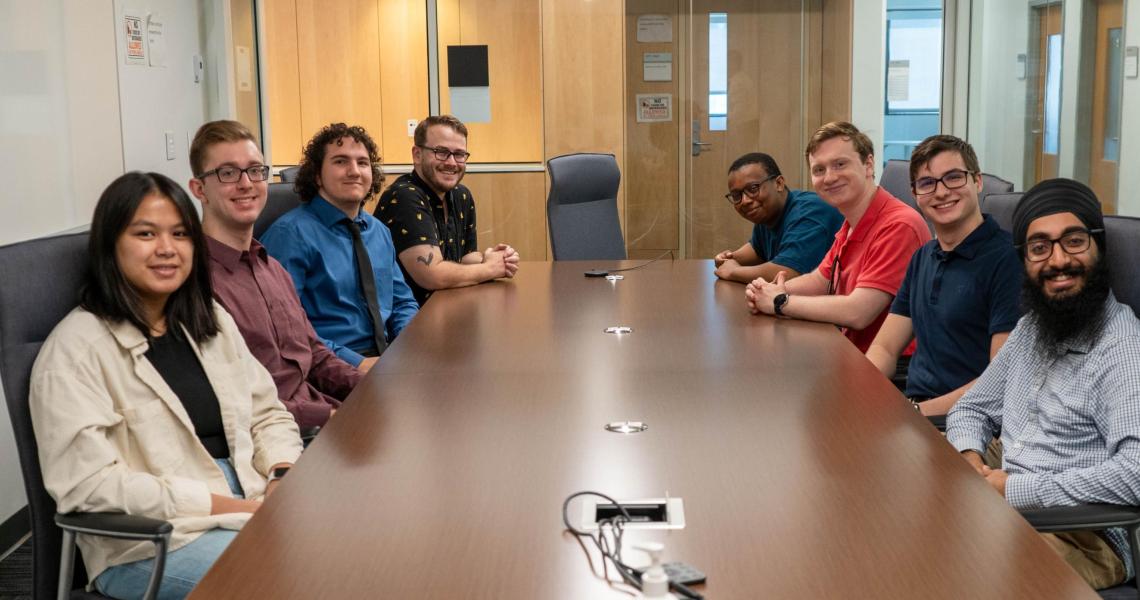 An image of 8 students around a conference table.