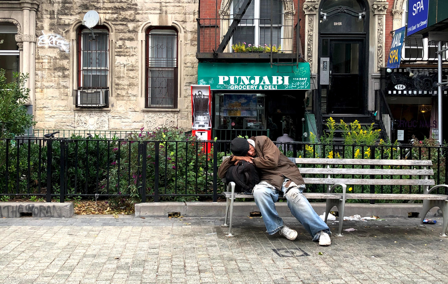 A person taking a nap on a bench outside of Punjabi Grocery & Deli in NYC's Lower East Side.